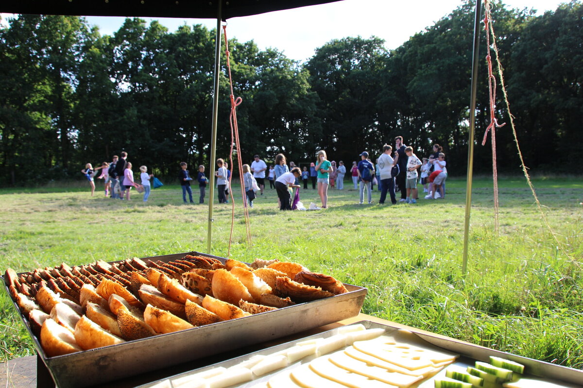 Büffet mit frischem Brot, Käse und Gemüse auf dem Zeltplatz, im Hintergrund Kinder und Betreuer auf der Wiese