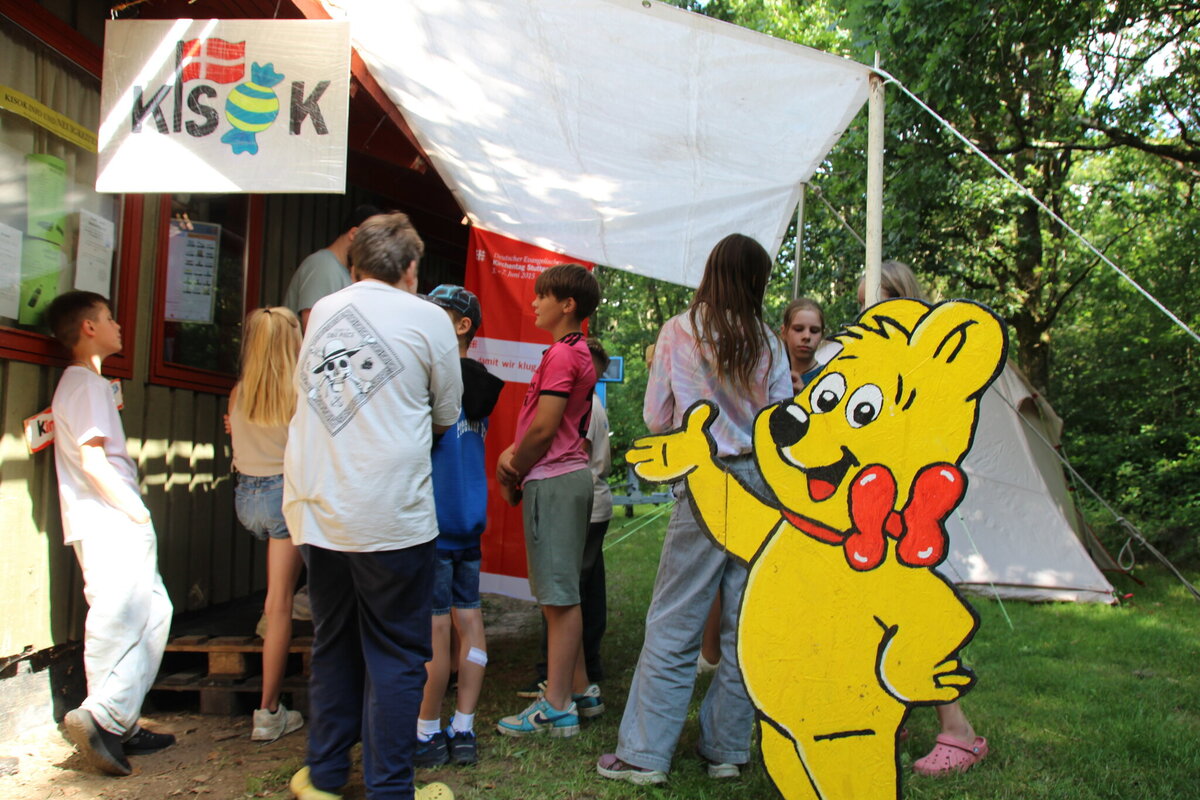 Kinder und Jugendliche an einem Kiosk mit Haribo-Bär-Schild