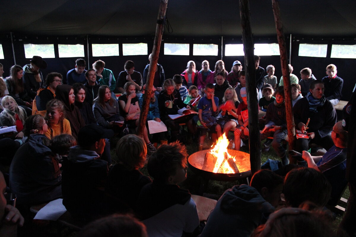 Große Gruppe sitzt abends um ein Lagerfeuer in einem Zelt