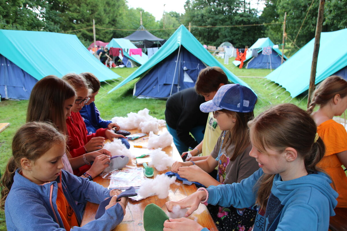 Kinder basteln gemeinsam an einem Tisch im Freien vor den Zelten