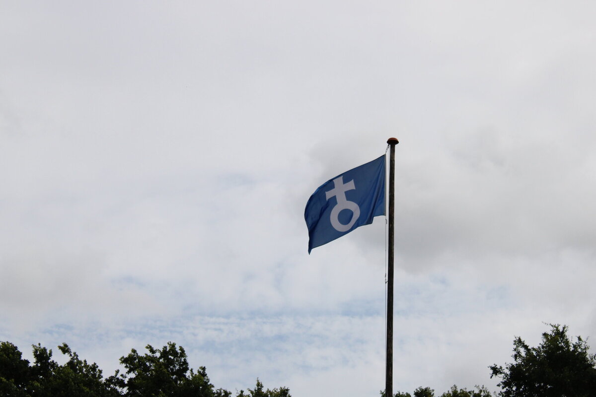 Blaue Fahne mit weißem Emblem weht am Mast